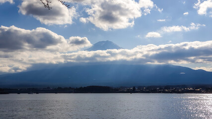 An idyllic view on Mt Fuji from the side of Kawaguchiko Lake, Japan. The mountain is hiding behind the clouds. Top of the volcano covered with a snow layer. Serenity and calmness. Calm lake's surface