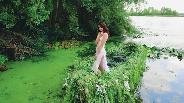 Fantasy happy brunette woman fashion model posing in boat, sexy white dress, slits on long legs. Fairy Girl princess. summer nature blue water lake green tree. Spring fresh plants. beauty river nymph
