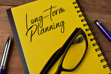 Top view of pen, eyeglasses and notebook written with LONG-TERM PLANNING
