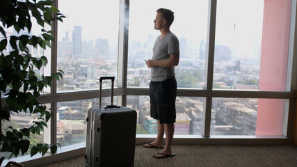 A man is enjoying smoking with wape in front of panoramic window with a luggage