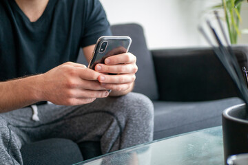 ソファーに座り携帯電話を見ながらくつろぐ男性の手元とインテリア