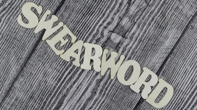 Swearword - concept design template on rustic wooden background with wavy line of alphabet letters and copyspace above and below. Rotation