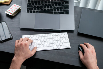 デスクに向かってキーボードをタイピングする男性の手