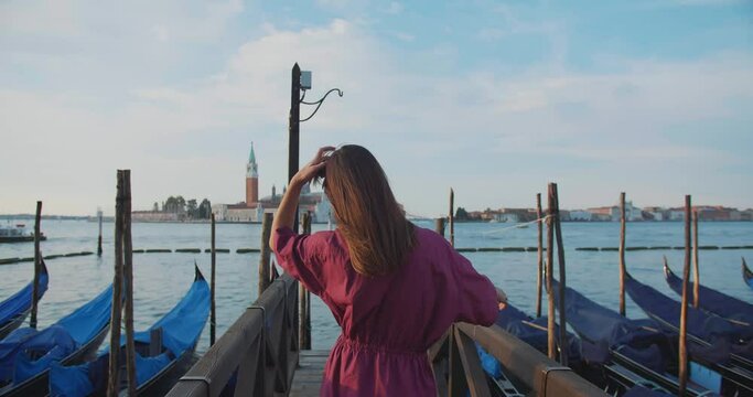 Camera follows beautiful happy brunette Caucasian tourist woman walk on famous gondola pier in Venice on summer trip.