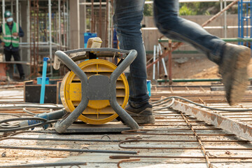 Yellow concrete vibrater on rebar for floor pouring frame in construction area, background with columnar and building condition during construction.