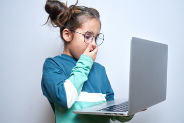 Shocked child girl with open mouth and bulging eyes looks at a computer laptop screen. Internet...