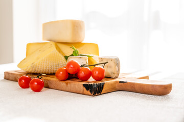 Homemade hard cheeses served on a wooden cutting board with tomatoes, side view.