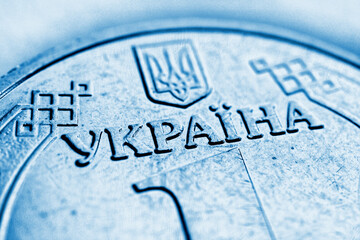 Translation of the inscription: Ukraine. Light blue background about economy or finance of Ukraine. A fragment of coin in 1 hryvnia. Focus on the name of the country, the coat of arms in blur. Macro