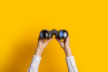 Fotobehang female hands hold black binoculars on a bright yellow background © Alex