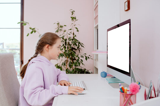 A teenage school aged girl uses a desktop computer while sitting at a desk in her room. She participates in remote learning and checks content posted by friends on social media.