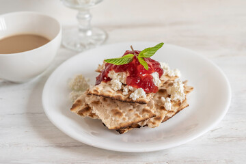 Breakfast ideas for Jewish holiday Pesach. Matzah bread, cottage cheese and strawberry sauce on white plate.