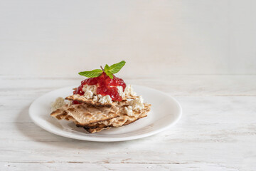 Matzah bread, cottage cheese and strawberry jam on white plate over wooden background with copy space.