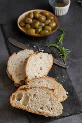 Italian sliced ciabatta bread on chopping board with herbs, extra virgin oil and marinated olives on dark grunge backdrop