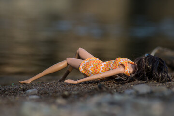 Portrait of mannequin doll lying on the sand in border river with her orange summer dress