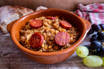 Migas Manchegas with chorizo in a clay pot, served with grapes, garlic and bread. It is a Spanish dish, traditional from Castilla la Mancha.