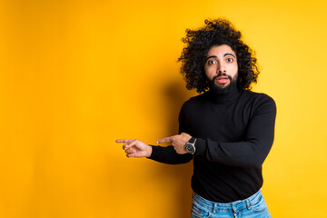 Attractive young african american guy worriedly points fingers to the side while standing on yellow background