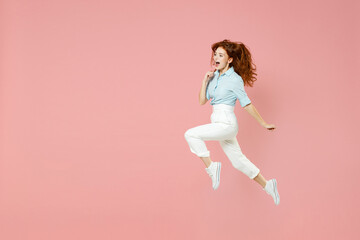 Fototapeta na wymiar Full length young student overjoyed excited fun caucasian happy redhead woman 20s wearing blue shirt pants jumping high running fast hurrying isolated on pastel pink color background studio portrait.