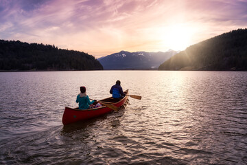 Fototapeta na wymiar Couple friends canoeing on a wooden canoe during a colorful sunny sunset. Cloudy Sky Artistic Render. Taken in Harrison River, East of Vancouver, British Columbia, Canada.