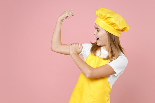 Teen strong sporty girl chef cook confectioner baker housewife in yellow apron white t-shirt cap put arm on biceps muscles on hand demonstrate strength isolated on pink background studio Food concept.
