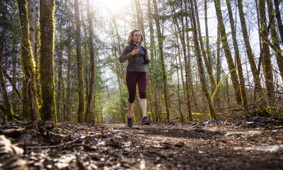Naklejka na ściany i meble Caucasian Woman Trail Running in the Green Forest surrounded by beautiful trees. Taken in Squamish, British Columbia, Canada.