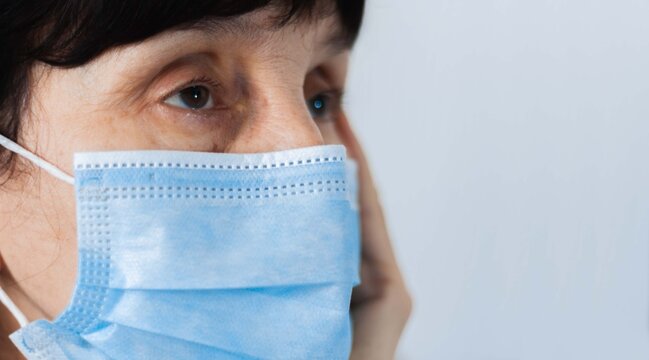 Coronavirus quarantine and Air pollution pm2.5 concept. Face of old sick woman wearing blue respirator mask for protect. Wuhan, China epidemic virus symptoms background.