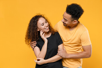 Young romantic couple friends together african pensive wistful dreamful woman man 20s in black yellow t-shirt boyfriend hug girlfiend look to each other isolated on orange background studio portrait.
