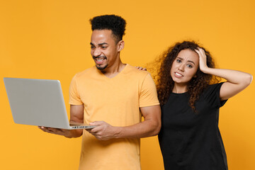 Young couple two friends together family african troubled disappointed man woman 20s wear black t-shirt hold laptop pc computer work online hold head isolated on yellow background studio portrait