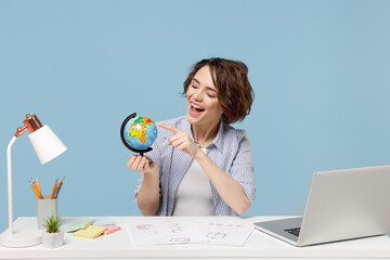 Young travel agent successful secretary employee business woman in casual shirt work at white office desk with pc laptop point finger on Earth world globe isolated on pastel blue background studio.