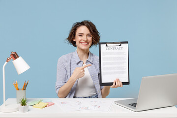 Young secretary successful employee business woman in shirt sit work at white office desk with pc laptop point index finger on clipboard with papers document isolated on pastel blue background studio.