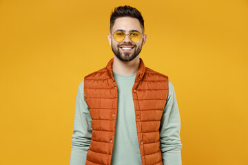 Young smiling happy friendly cheerful fun caucasian man 20s years old wearing orange vest mint sweatshirt glasses looking camera isolated on yellow background studio portrait People lifestyle concept.
