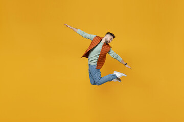Fototapeta na wymiar Full length young excited happy fun caucasian cheerful overjoyed man 20s years old in orange vest mint sweatshirt jump high spreading outstretched hand look aside isolated on yellow background studio
