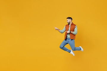 Fototapeta na wymiar Full length side view young happy fun caucasian man 20s wear orange vest mint sweatshirt jump high point index finger aside on copy space workspace mock up area isolated on yellow background studio.