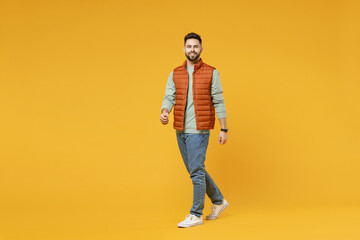 Fototapeta na wymiar Full length young smiling happy confident smiling cheerful fun caucasian man 20s years old wear orange vest mint sweatshirt walking going looking camera isolated on yellow background studio portrait