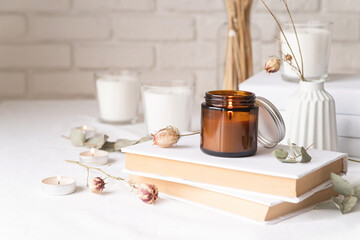 Beautiful burning candles with eucalyptus leaves and dry flowers on pile of white books