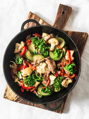 Quick beef stew with zucchini, cauliflower, sweet pepper, kale in a cast-iron pan on a light background, top view
