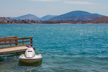 Fototapeta na wymiar Beautiful landscape – summer resort – sea bay with turquoise clear water, wooden pier and white jet ski, blue sky and mountains on the horizon. Saranda, Albania.