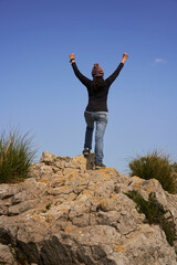 Woman with arms outstretched towards the sky, on top of a mountain