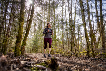 Caucasian Woman Trail Running in the Green Forest surrounded by beautiful trees. Taken in Squamish, British Columbia, Canada.