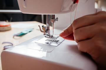 Closeup hands inserting thread into sewing machine needle