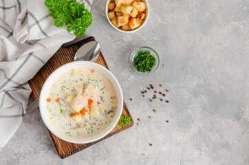 Salmon soup with cream, potatoes, carrots, herb and croutons in a bowl on a gray concrete...