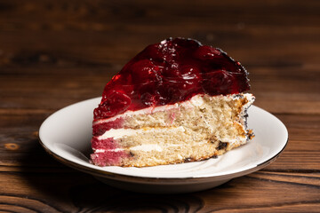 a piece of cherry cake on a white plate on a wooden table. Black background.