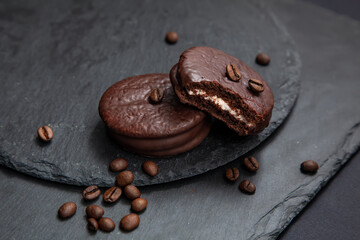 A few sweet Choco pie desserts on a black stone board background among scattered coffee beans.