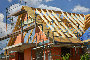 Gerüst am hölzernen Dachstuhl eines neu gebauten Mehrfamilien-Wohnhauses im Rohbau in einem Neubaugebiet