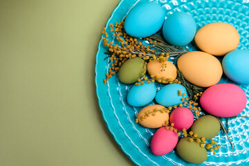 Fototapeta na wymiar Turquois dish with painted blue, green, yellow, and pink eggs with mimosa