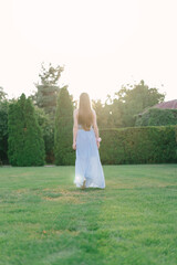 Young beautiful woman with long fair hair in long light blue chiffon dress, walking in the green...