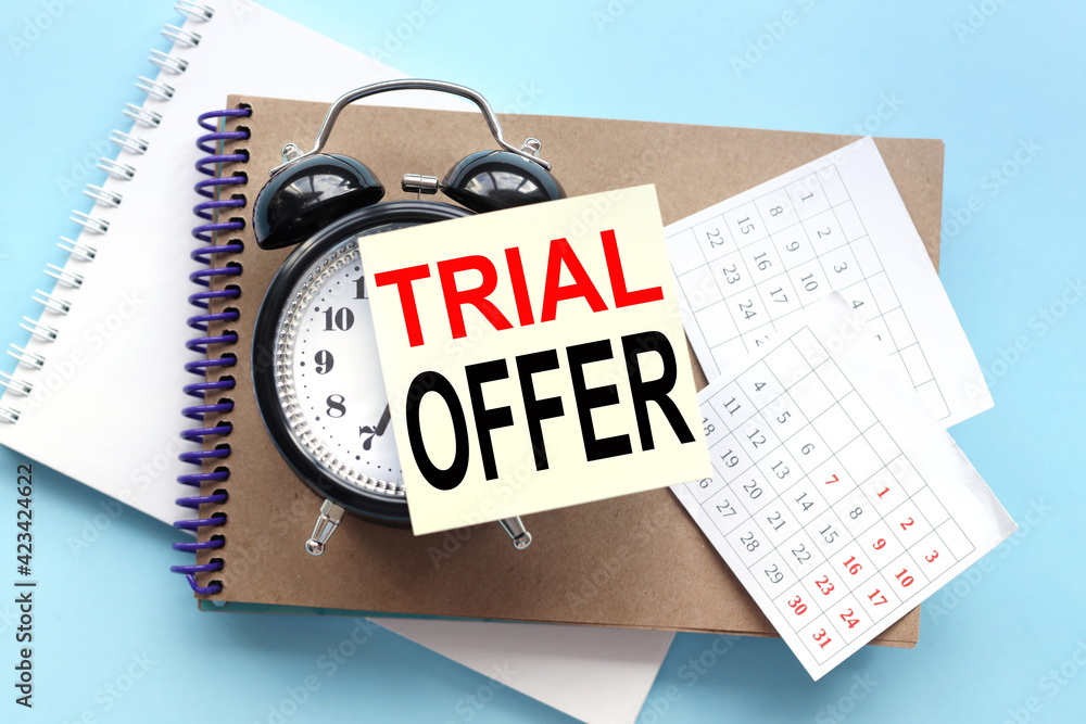 Poster trial offer. text on the sticker attached to the alarm clock. alarm clock on notepad on blue backgro