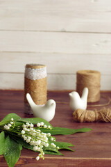 A bouquet of white lilies of the valley lies on the table next to jars and figurines of birds