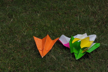 Kolorowe papierowe samolociki leżą na zielonej trawie