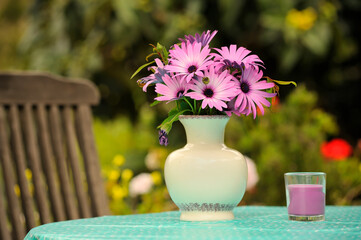 Garden table with bouquet of purple cape marguerite (Dimorphotheca ecklonis) flowers in white vase and purple candle.