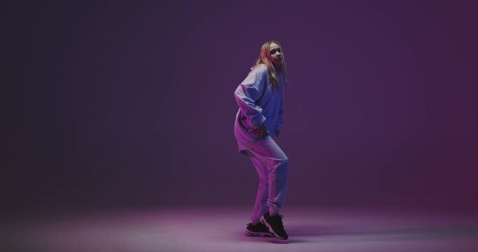 4k video of a stylish young girl, cool dancing in a hoodie hip hop dance on a neon studio background